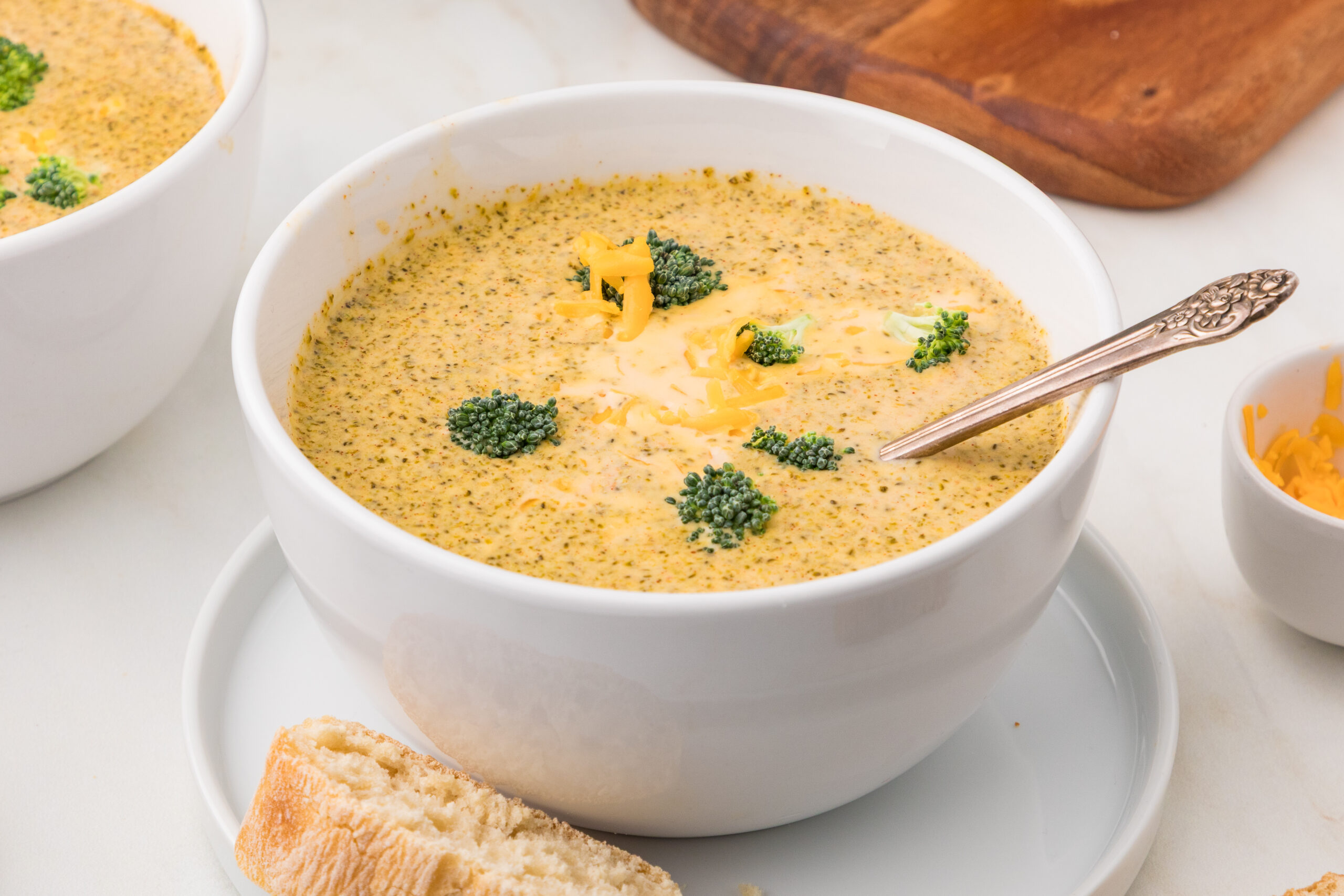 A bowl of creamy slow cooker broccoli cheddar parmesan soup topped with melted cheese.