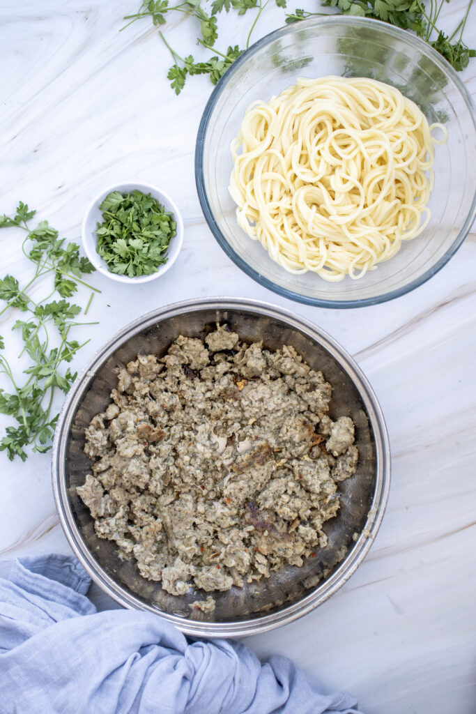Italian sausage in a pan and cooked spaghetti in a bowl