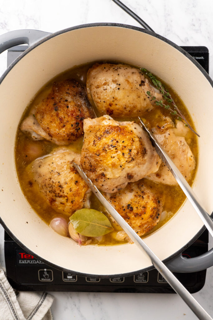 chicken thighs in a Dutch oven with a tong