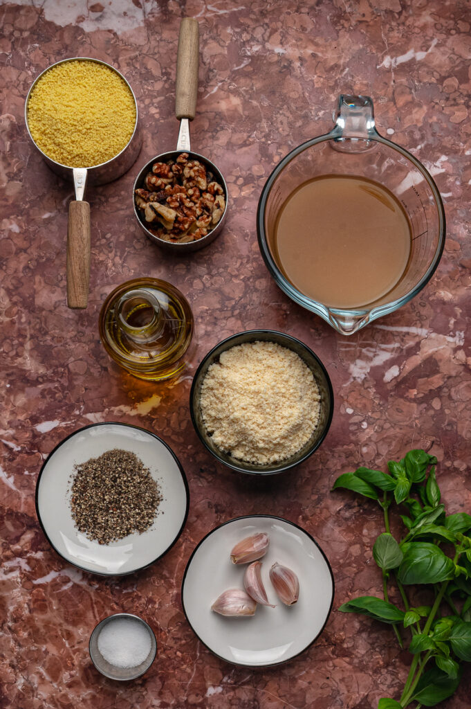 Fresh basil, walnuts, garlic, olive oil, and Parmesan on a kitchen counter